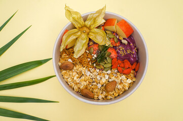 Top view Acai smoothie bowl with superfoods. Smoothie bowl topped with Strawberry ,and granola almonds on color paper background 