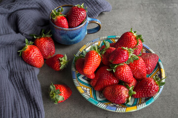 Fruit diet concept. Blue ceramic plate and cup full of fresh juicy strawberries on a table. Dark gray textured background. Eating fresh concept. 
