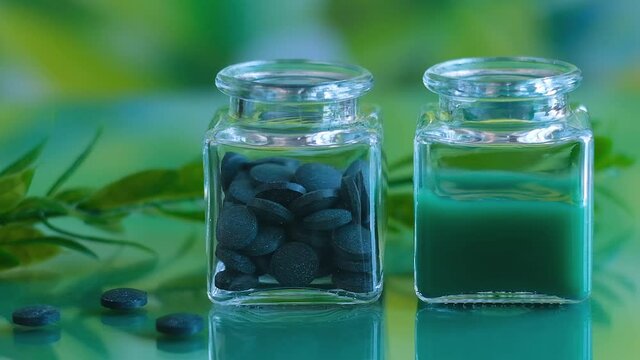 In one glass jar of spirulina tablets and in the other drips a solution of chlorella powder. No people, close-up
