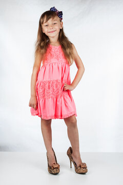 Cute little girl in high-heeled shoes posing on a white background.