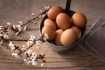 Tin vase with eggs and cherry branches on rough wooden table