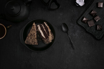 Pieces of cake on a black plate, tea with sweets on a dark background. Top view