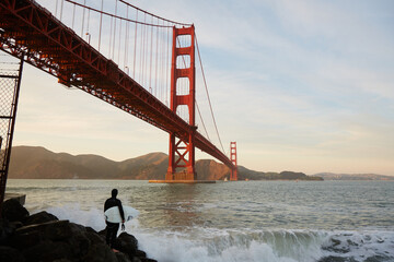 A surfer stands in front of the Golden Gate Bridge in San Francisco - California - USA.