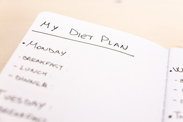 Diet plan: planning of the weekly diet, with the foods to eat during the week, written on a white notebook with black ink.