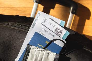 Post covid 19 travel concept, vaccination and immunity pass implementation. Airline boarding pass, protective face mask and a biometric passport on a suitcase bag