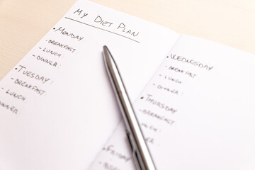 Diet plan: planning of the weekly diet, with the foods to eat during the week, written on a white notebook with black ink.