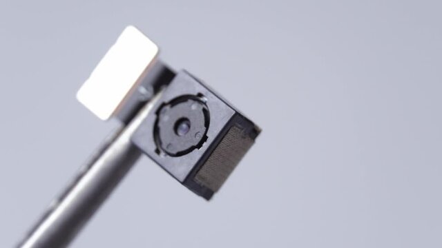 Close-up on the mobile phone camera module. Close-up tweezers or clip holds smartphone lens in studio shot white white background