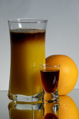 Brown, herbal layer drink with orange juice. Single liqueur shot and fruit on the side. Reflection on the bottom and gradient background