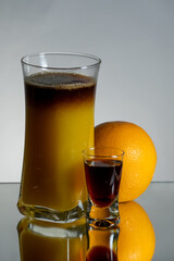 Brown, herbal layer drink with orange juice. Single liqueur shot and fruit on the side. Reflection on the bottom and gradient background