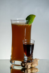 Brown herbal alcohol drink with ginger beer and fresh grated ginger. Lemon zest on the top of a glass. Single shot and ginger around. Reflection on the bottom and gradient background
