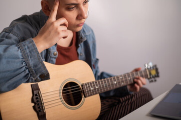 Young woman is learning to play the guitar online. Remote music lessons on a laptop