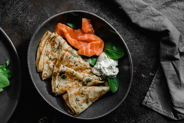 Thin pancakes with herbs, salmon and cream cheese on a plate. crepes