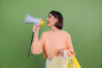 Young woman in casual peach sweater isolated on green olive color background shout in megaphone...