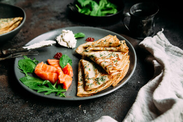 Thin pancakes with herbs, salmon and cream cheese on a plate