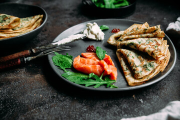 Thin pancakes with herbs, salmon and cream cheese on a plate