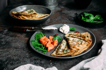 Thin pancakes with herbs, salmon and cream cheese on a plate