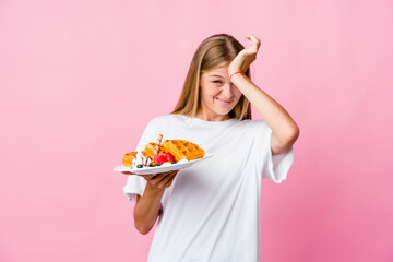 Young russian woman eating a waffle isolated forgetting something, slapping forehead with palm and closing eyes.