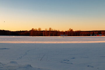 A winter country landscape with hare tracks on snowy field in sunset.