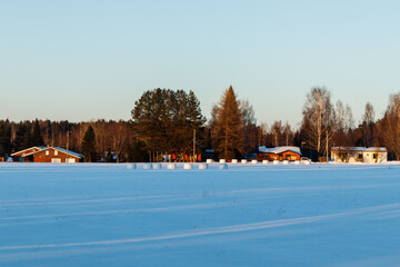 Fototapeta na wymiar A winter country landscape with hay bales on snowy field in sunset.