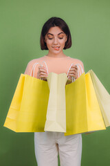 Young woman in casual peach sweater isolated on green olive color background holding shopping bags...
