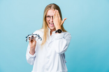 Young russian optometrist woman on blue having fun covering half of face with palm.