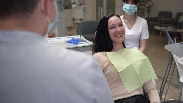 A young Caucasian woman at the doctor's appointment sits in a dental chair and has fun talking with the doctor. Dental health.