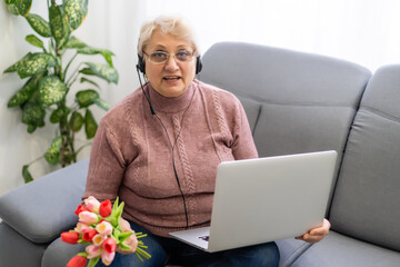 Cropped shot of a beautiful elderly woman using laptop computer while sitting with flowers