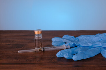 A Vaccine in vial , medical glove and syringe close-up on a wooden table blue backgraund, medical...