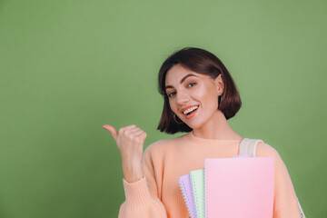 Young woman in casual peach sweater isolated on green olive color background with notebooks...