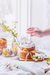 Traditional ukrainian easter cake with white swiss meringue. New cruffin cake trend 2021. Spring cherry blossom and colorful painted eggs. Person decorates cake with hand. Free copy space