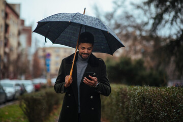 Afro businessman on rainy day using phone