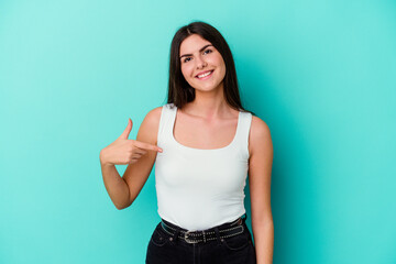 Young caucasian woman isolated on blue background person pointing by hand to a shirt copy space, proud and confident