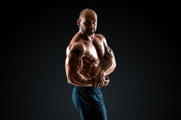 Fototapeta na wymiar Male bodybuilder with light stubble with a naked torso posing against a dark background. The concept of a fitness club, doing sports, weightlifting. Copy space.