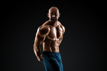 Fototapeta na wymiar Male bodybuilder with light stubble and bare torso shows muscularity against a dark background. The concept of a fitness club, doing sports, weightlifting. Copy space.