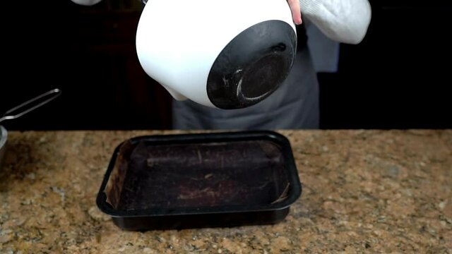 Slow motion footage of chocolate cake brownie mix being poured into a baking tray. Home baking food concept.