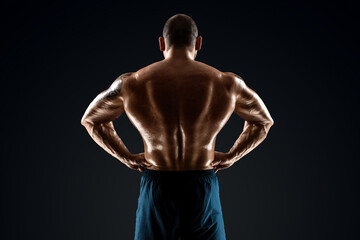 Fototapeta premium Male bodybuilder with light stubble and bare torso shows muscularity against a dark background. The concept of a fitness club, doing sports, weightlifting. Copy space.