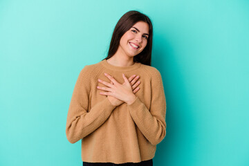 Young caucasian woman isolated on blue background has friendly expression, pressing palm to chest. Love concept.