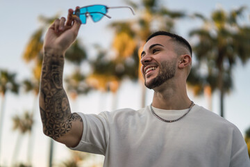 Chico joven atractivo con tatuajes en zona con palmeras