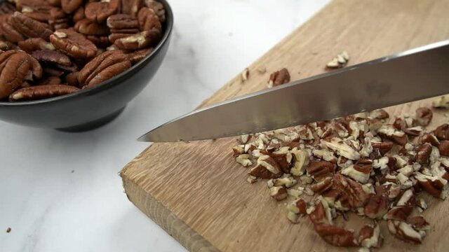 Pecans being chopped with large knife on wooden chopping board in slow motion. Pecan nuts food preparation concept.