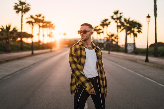 Chico joven guapo en mitad de carretera al atardecer con camisa amarilla