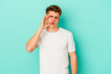 Young caucasian man isolated on blue background with fingers on lips keeping a secret.