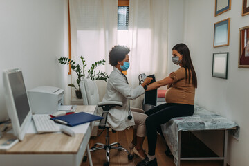Doctor with a pregnant woman wearing medical masks during an examinations - Powered by Adobe