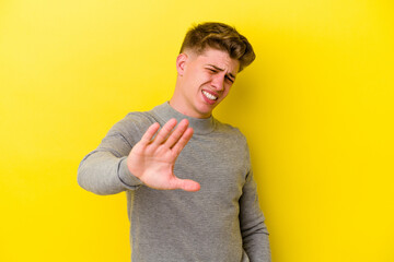 Young caucasian man isolated on yellow background rejecting someone showing a gesture of disgust.