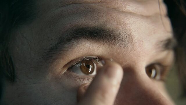 Close-up slow motion young man gently puts a contact lens on his brown eye. Installing a contact lens for vision correction. Cool color 