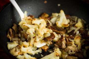 fried cauliflower with wild porcini mushrooms and onions in a pan