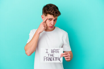 Young caucasian man holding a I hate the pandemic placard isolated on blue background