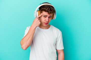 Young caucasian man listening to music with headphones isolated on blue background showing a disappointment gesture with forefinger.