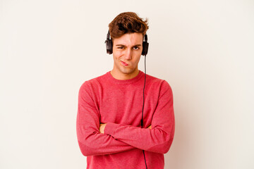 Young caucasian man listening to music isolated on white background frowning face in displeasure, keeps arms folded.