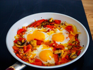 Shakshuka - fried eggs with sausages and vegetables in frying pan
