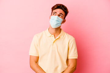 Young caucasian man wearing a protection for coronavirus isolated on pink background dreaming of...